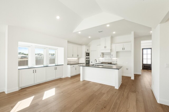 kitchen featuring backsplash, vaulted ceiling, sink, white cabinetry, and oven