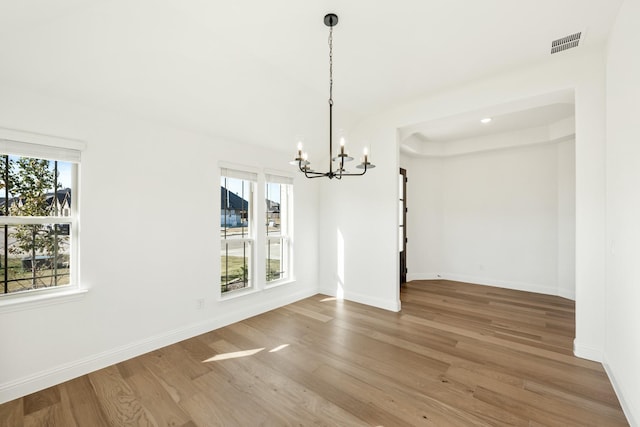 unfurnished dining area with a healthy amount of sunlight, hardwood / wood-style floors, and a chandelier