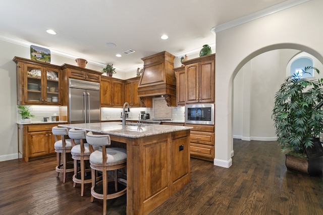 kitchen featuring sink, built in appliances, tasteful backsplash, and an island with sink