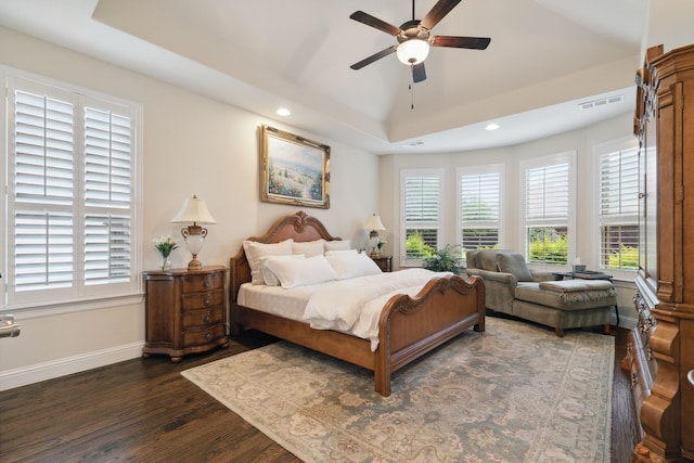 bedroom featuring a tray ceiling, multiple windows, ceiling fan, and dark hardwood / wood-style floors