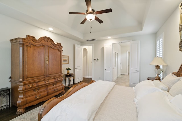 bedroom featuring ceiling fan, light wood-type flooring, and a tray ceiling