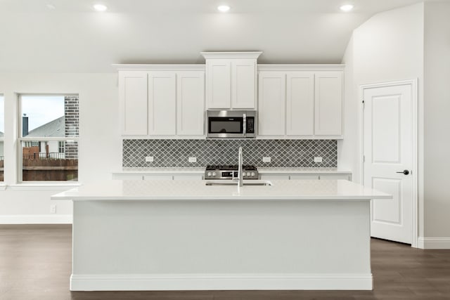 kitchen featuring an island with sink, wood-type flooring, white cabinetry, appliances with stainless steel finishes, and decorative backsplash