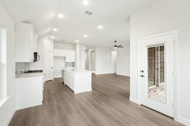 kitchen with decorative backsplash, light hardwood / wood-style floors, white cabinetry, an island with sink, and sink