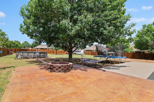 view of patio with a fire pit, a fenced in pool, and a trampoline