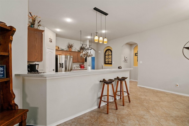 kitchen with kitchen peninsula, light tile patterned floors, decorative light fixtures, stainless steel fridge with ice dispenser, and a breakfast bar area