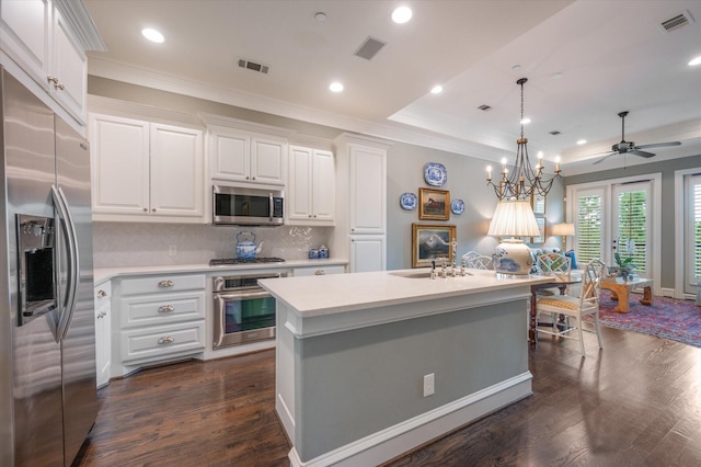 kitchen with appliances with stainless steel finishes, a kitchen island with sink, pendant lighting, and white cabinets