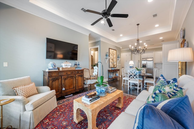 living room with crown molding, dark wood-type flooring, ceiling fan with notable chandelier, and a tray ceiling