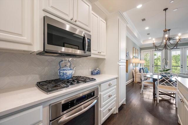 kitchen featuring pendant lighting, white cabinets, appliances with stainless steel finishes, dark wood-type flooring, and decorative backsplash