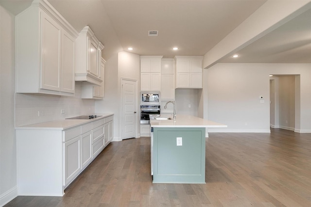 kitchen with white cabinets, built in microwave, black electric stovetop, and a center island with sink