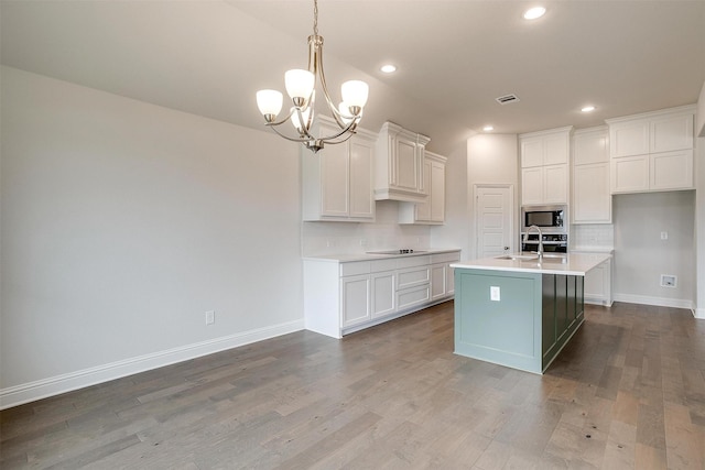 kitchen featuring stainless steel microwave, tasteful backsplash, pendant lighting, sink, and a kitchen island with sink