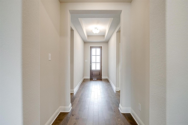 doorway with dark wood-type flooring and a tray ceiling