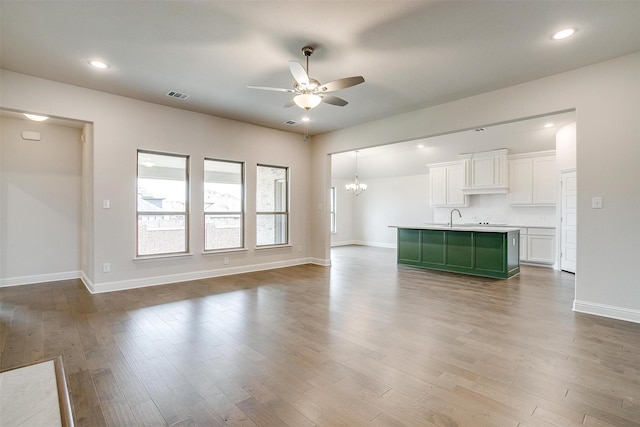 unfurnished living room featuring ceiling fan with notable chandelier, sink, and light wood-type flooring