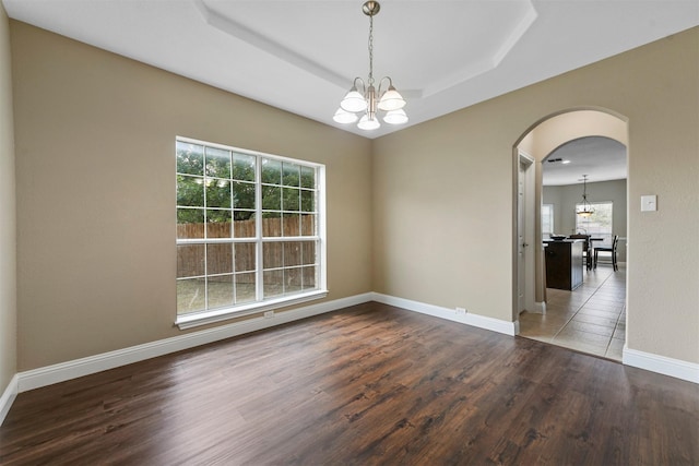 empty room with a chandelier, dark hardwood / wood-style flooring, and a tray ceiling