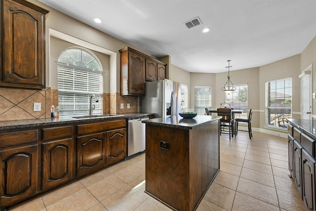 kitchen featuring appliances with stainless steel finishes, backsplash, sink, light tile patterned floors, and a center island