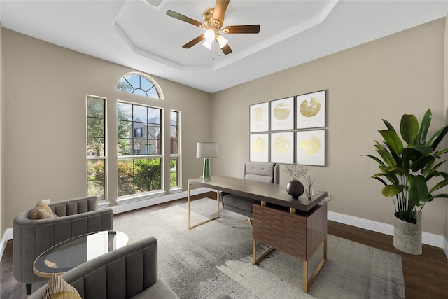 home office with a tray ceiling, ceiling fan, and dark wood-type flooring