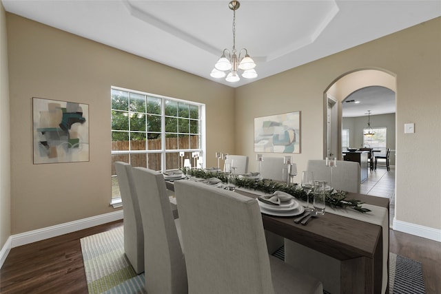 dining space featuring hardwood / wood-style flooring, a raised ceiling, and a notable chandelier