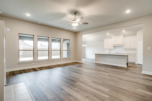 unfurnished living room featuring light wood-type flooring, sink, and ceiling fan with notable chandelier