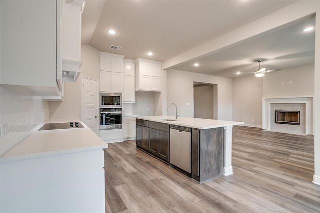 kitchen featuring white cabinets, black appliances, a kitchen island with sink, ceiling fan, and a tiled fireplace