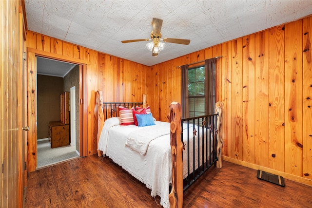 bedroom featuring ceiling fan, dark wood-type flooring, and wood walls