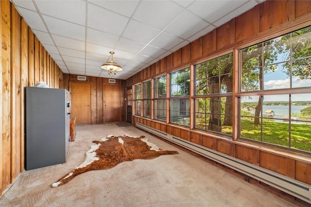 unfurnished sunroom featuring a paneled ceiling, a water view, plenty of natural light, and a baseboard heating unit