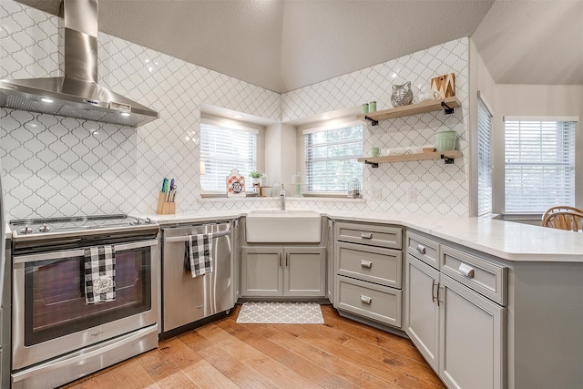 kitchen featuring appliances with stainless steel finishes, light hardwood / wood-style floors, kitchen peninsula, sink, and wall chimney range hood