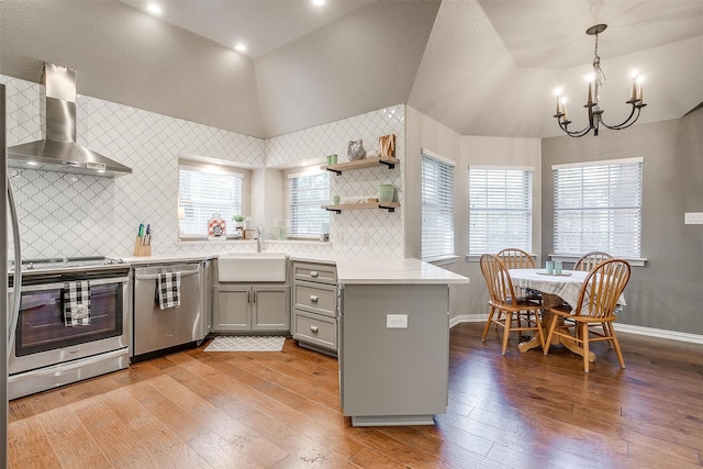 kitchen with lofted ceiling, wall chimney exhaust hood, appliances with stainless steel finishes, gray cabinets, and a sink