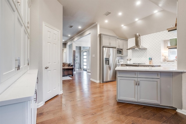 kitchen with stainless steel appliances, gray cabinets, backsplash, wall chimney range hood, and light wood-type flooring