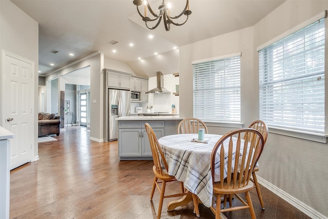 dining space with an inviting chandelier, light wood-type flooring, and vaulted ceiling