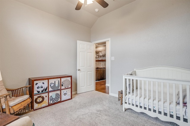 carpeted bedroom with ceiling fan, a nursery area, and vaulted ceiling