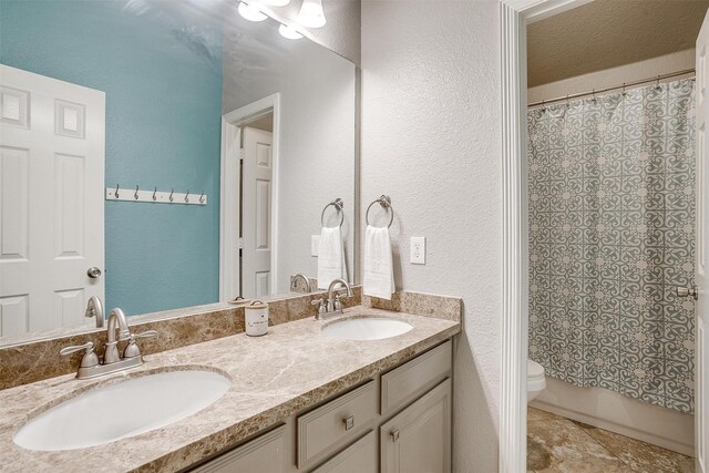 bathroom with a textured wall, double vanity, a sink, and toilet