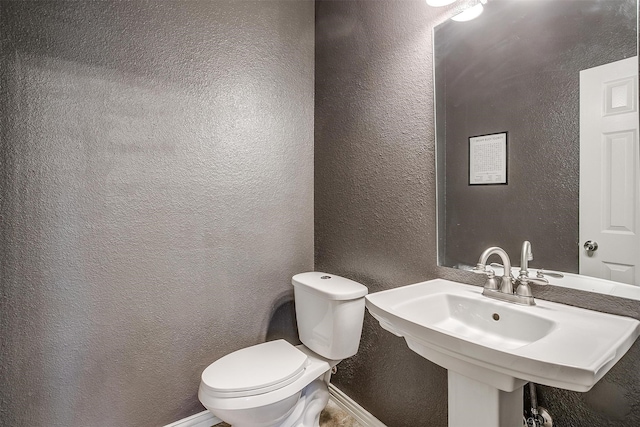 half bathroom featuring toilet, a textured wall, and a sink