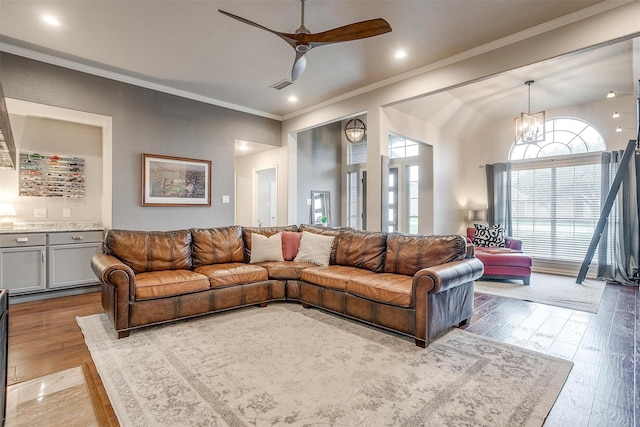 living room with ceiling fan with notable chandelier, light wood-type flooring, crown molding, and lofted ceiling