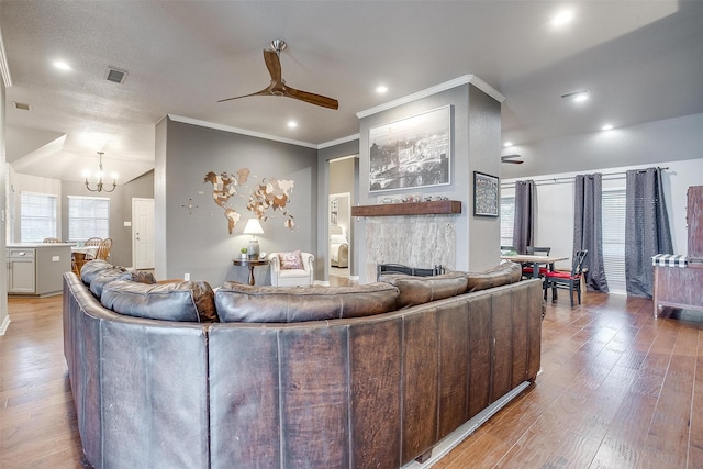 living area featuring a fireplace, wood-type flooring, visible vents, ornamental molding, and ceiling fan with notable chandelier