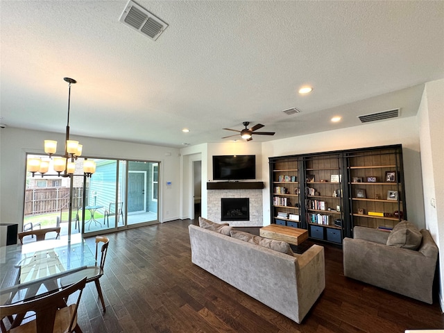 living room with dark hardwood / wood-style floors, ceiling fan with notable chandelier, a fireplace, and a textured ceiling