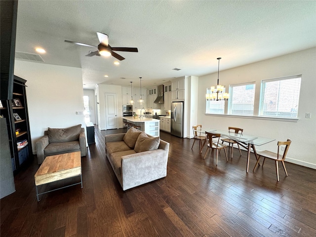 living room with ceiling fan with notable chandelier, dark hardwood / wood-style flooring, and a textured ceiling