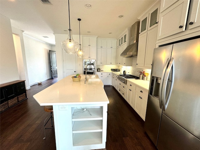 kitchen featuring appliances with stainless steel finishes, wall chimney range hood, a center island with sink, and dark wood-type flooring