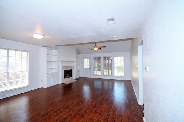 unfurnished living room featuring dark hardwood / wood-style flooring, a textured ceiling, ceiling fan, built in features, and a fireplace