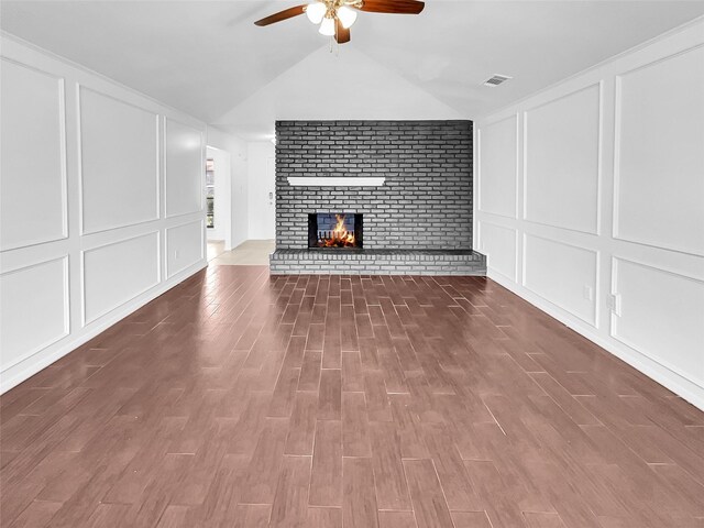 unfurnished living room featuring dark hardwood / wood-style floors, ceiling fan, vaulted ceiling, a fireplace, and brick wall