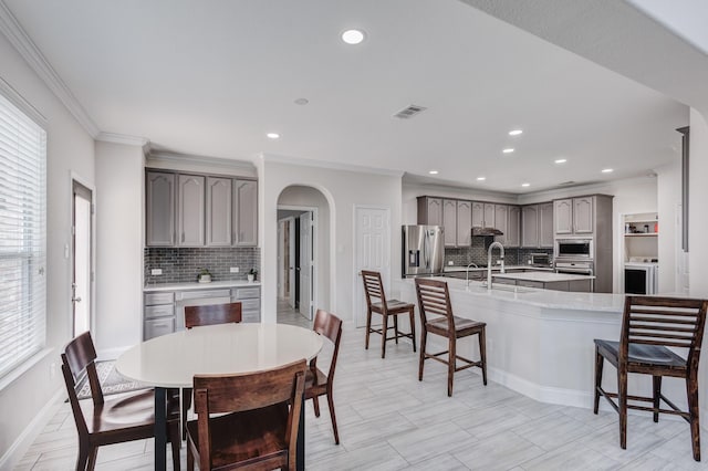 kitchen featuring sink, gray cabinetry, a kitchen bar, stainless steel appliances, and crown molding