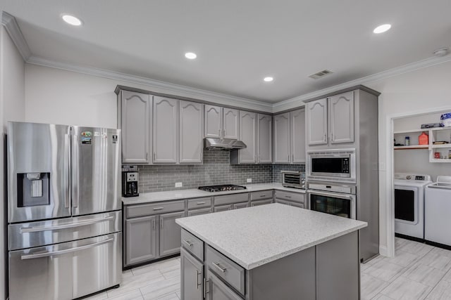 kitchen with crown molding, appliances with stainless steel finishes, a kitchen island, washing machine and dryer, and backsplash