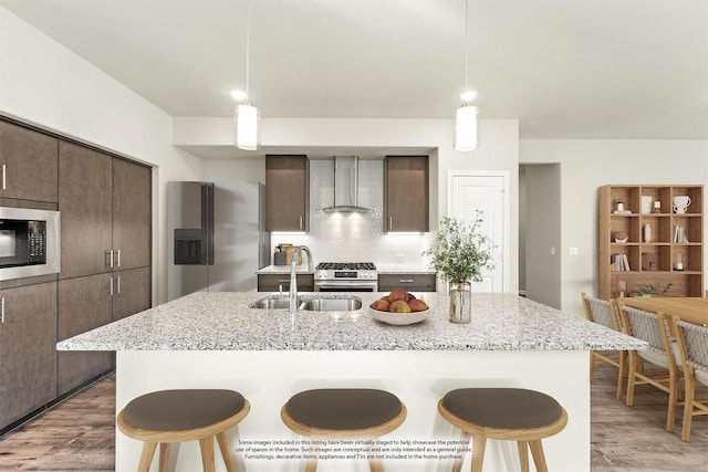 kitchen featuring backsplash, stainless steel appliances, a kitchen island with sink, sink, and wall chimney range hood