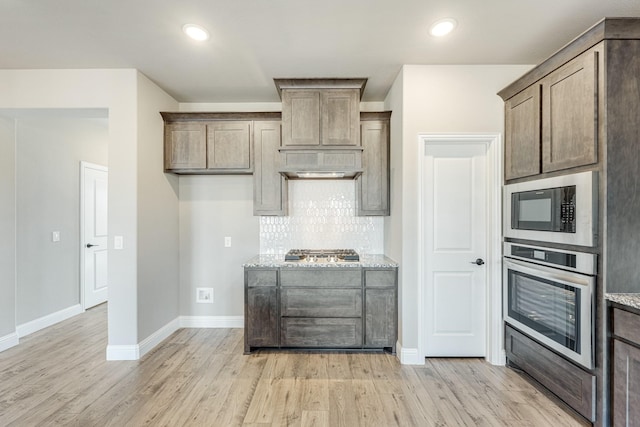 kitchen featuring decorative backsplash, appliances with stainless steel finishes, light hardwood / wood-style flooring, and light stone counters