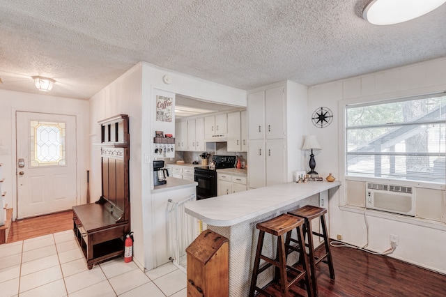 kitchen with black electric range oven, a healthy amount of sunlight, a breakfast bar, and white cabinetry