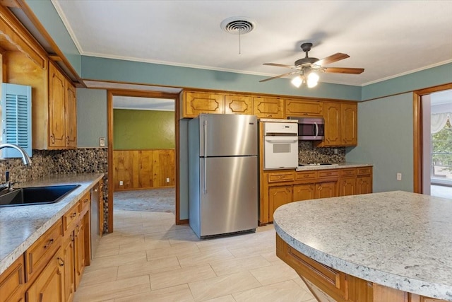 kitchen featuring stainless steel appliances, decorative backsplash, crown molding, ceiling fan, and sink