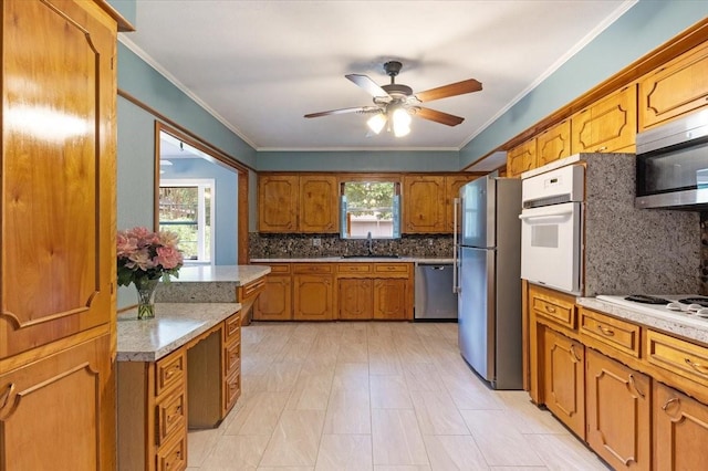 kitchen with appliances with stainless steel finishes, ceiling fan, ornamental molding, sink, and tasteful backsplash