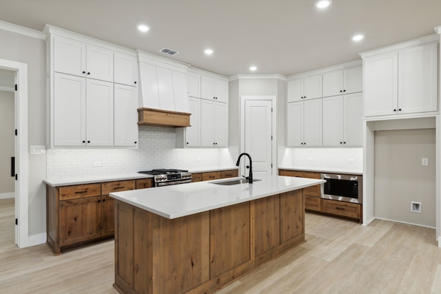 kitchen featuring white cabinets, high end stainless steel range, an island with sink, and sink