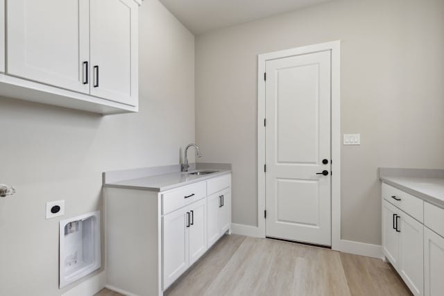 clothes washing area with hookup for an electric dryer, light wood-type flooring, cabinets, and sink