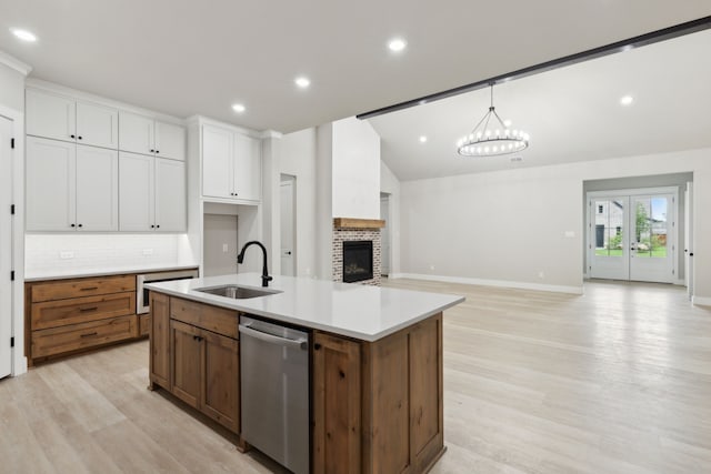 kitchen with white cabinetry, sink, an inviting chandelier, stainless steel dishwasher, and a center island with sink