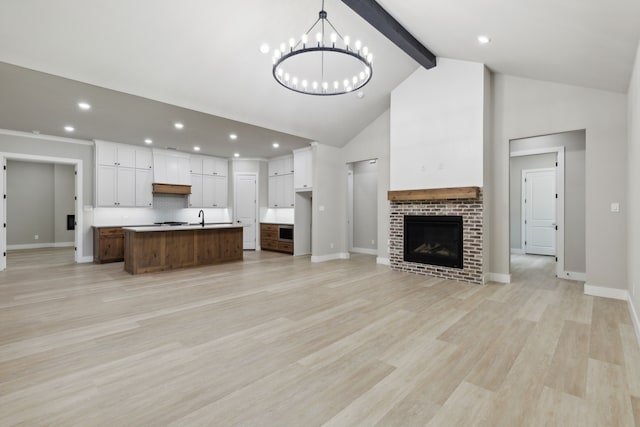 unfurnished living room with beam ceiling, a brick fireplace, high vaulted ceiling, a chandelier, and light hardwood / wood-style floors