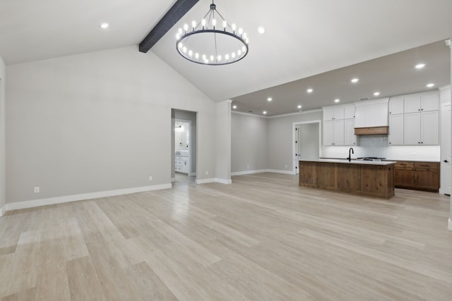 kitchen featuring an inviting chandelier, light hardwood / wood-style flooring, an island with sink, beamed ceiling, and white cabinetry